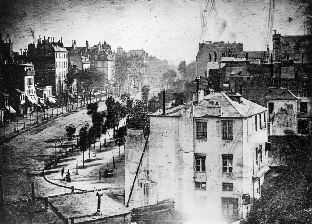 (Photo and following caption courtesy: https://en.wikipedia.org/wiki/History_of_photography "Boulevard du Temple", a daguerreotype made by Louis Daguerre in 1838, is generally accepted as the earliest photograph to include people. It is a view of a busy street, but because the exposure time was at least ten minutes the moving traffic left no trace. Only the two men near the bottom left corner, one apparently having his boots polished by the other, stayed in one place long enough to be visible.